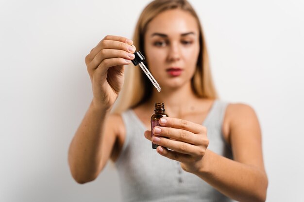 Girl holding pipette with oil facial serum in hands for acne treatment and wrinkle smoothing Girl with face serum making beauty procedure on white background