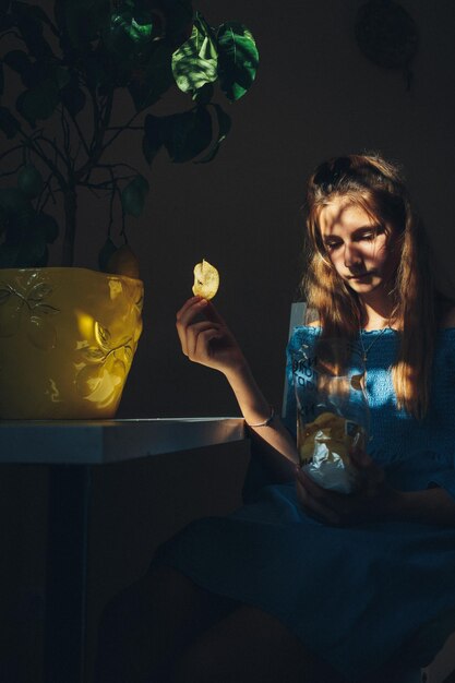 Photo girl holding potato chip sitting at home