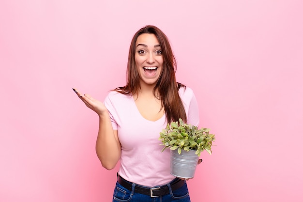 鉢植えの植物を保持している女の子は興奮して驚いた表情で驚いた