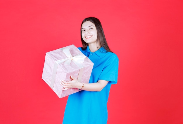 흰색 리본으로 포장된 보라색 선물 상자를 들고 있는 소녀