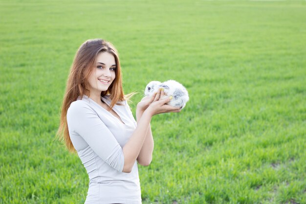 緑の牧草地にいる間ウサギを持って女の子。