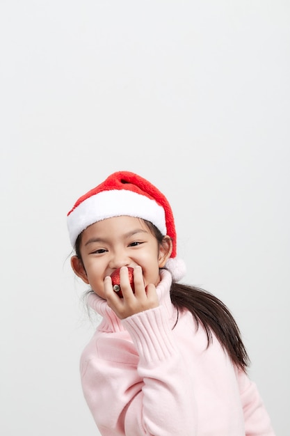 Girl holding a red christmas ball in sweater and santa hat