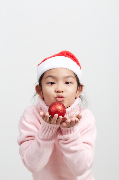 Girl holding a red christmas ball in sweater and santa hat