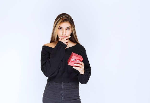Girl holding a red gift box and thinking or hesitating. High quality photo