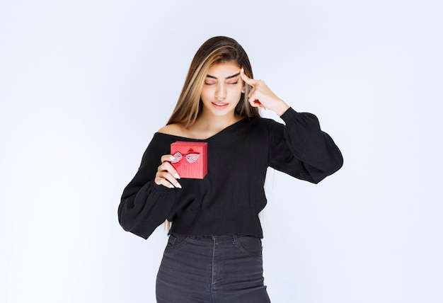 Girl holding a red gift box and thinking or hesitating. High quality photo