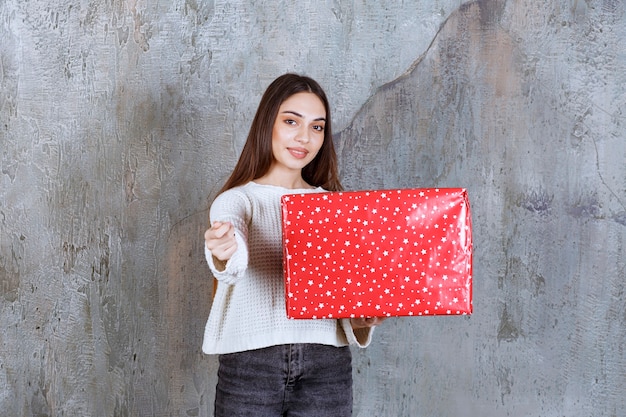 Girl holding a red gift box with white dots on it and asking for payment.