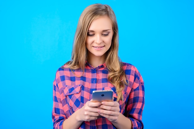 Ragazza che tiene smartphone in mani su sfondo blu isolato