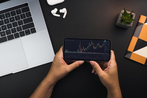 Girl holding a smartphone with financial stock market graph on the screen on black background table Office environment Stock Exchange