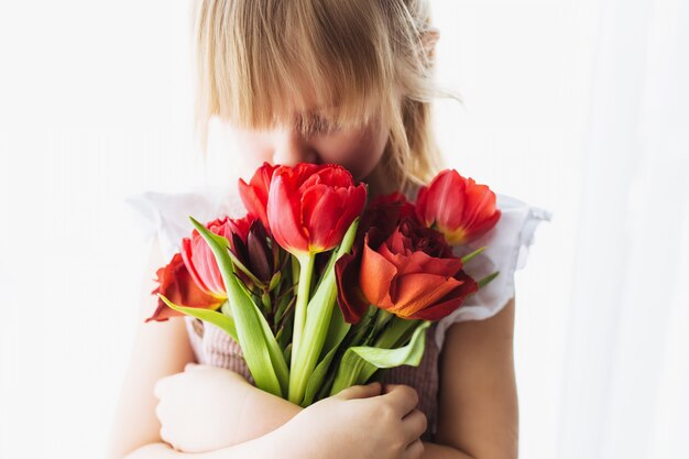 girl holding and sniffing bouquet of red tulip flowers