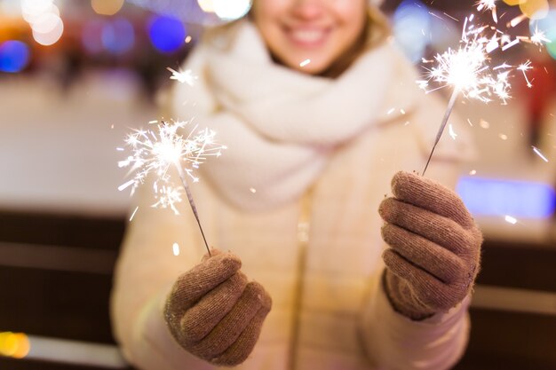 Foto ragazza con una stella filante in mano. sfondo della città invernale all'aperto, neve, fiocchi di neve.