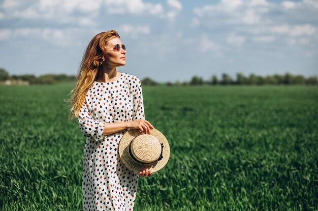 Girl holding a straw hat. Young happy woman in green field. Green grass and blue sky behind. Atmospheric summer young girl in green grass field