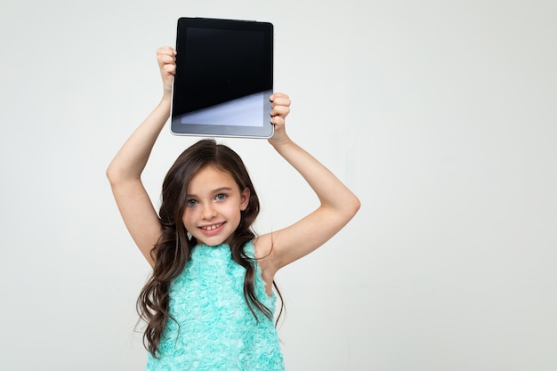 Photo girl holding a tablet with a blank screen over her head to insert a web page or advertisement on a white wall