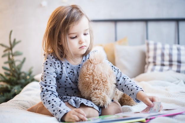 Girl holding a teddy bear on the bed at Christmas