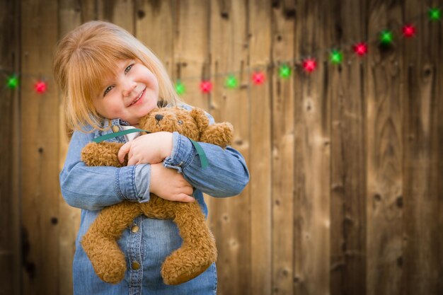 クリスマスのライトで森の背景の前でテディベアを抱いている女の子