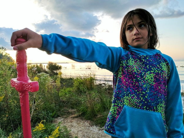 Foto ragazza con una spada giocattolo in piedi sul campo contro il cielo