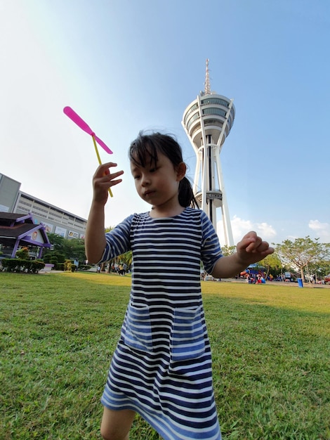 Girl holding toy while standing on grass against sky