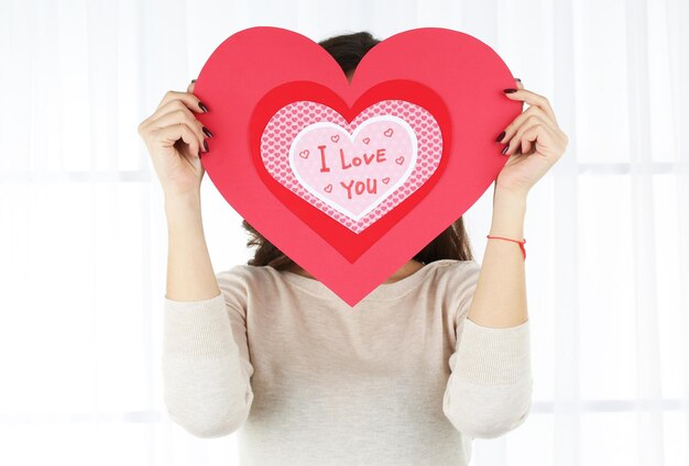 Girl holding Valentine card on bright background