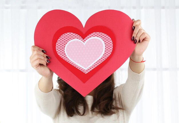 Girl holding Valentine card on bright background