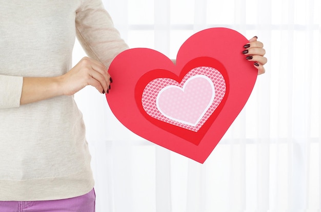 Girl holding Valentine card on bright background