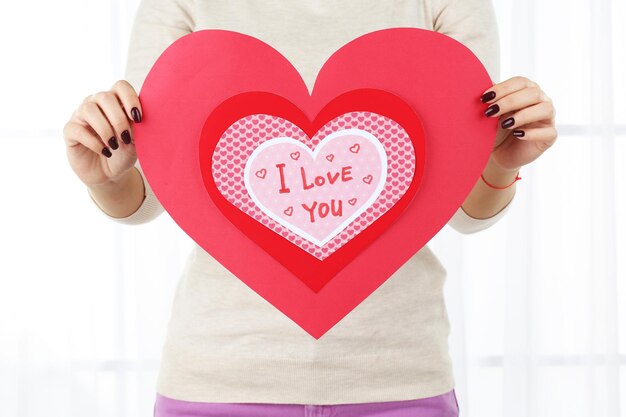 Girl holding Valentine card on bright background