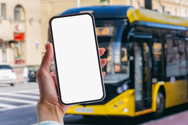 写真 バス停でバスを背景に、白い画面が表示されたスマートフォンのモックアップを手に持つ女の子