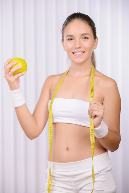 The girl holds an apple in his hands and a centimeter.