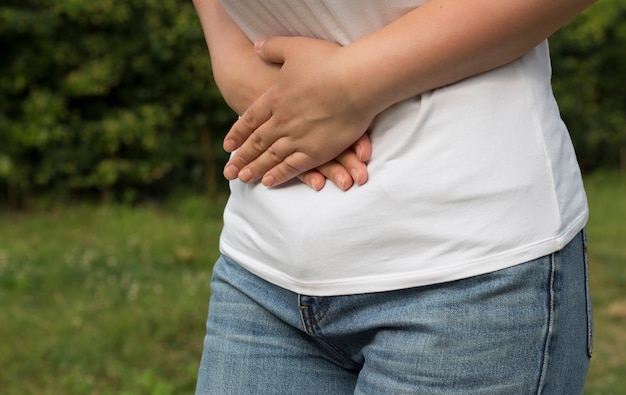 The girl holds on to the belly with both hands on the street, on a green background.