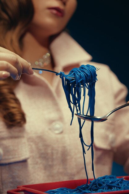 The girl holds blue spaghetti on a fork holding them with a spoon