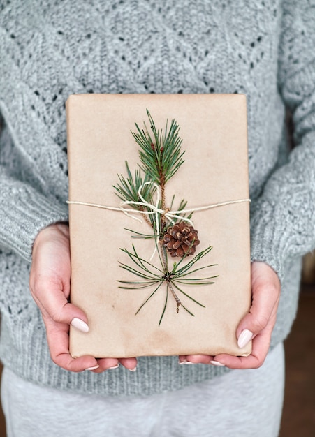 La ragazza tiene un libro per un regalo avvolto in carta artigianale decorata con un ramo di abete con un cono