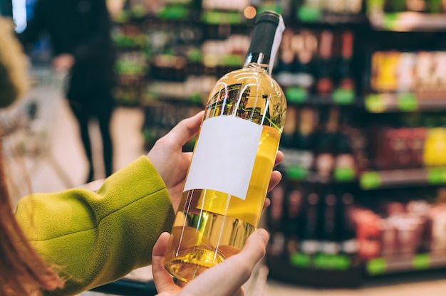 A girl holds a bottle of wine in the store.