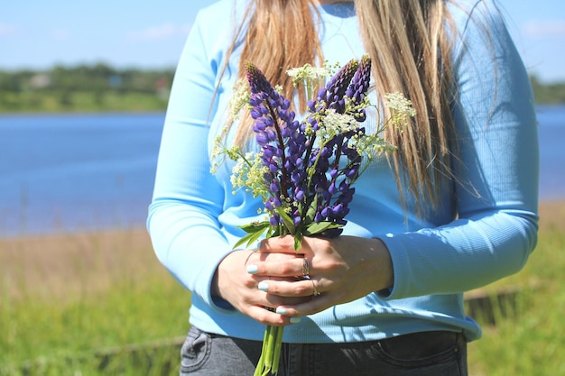 A girl holds a bouquet of wildflowers standing on the bank of the river