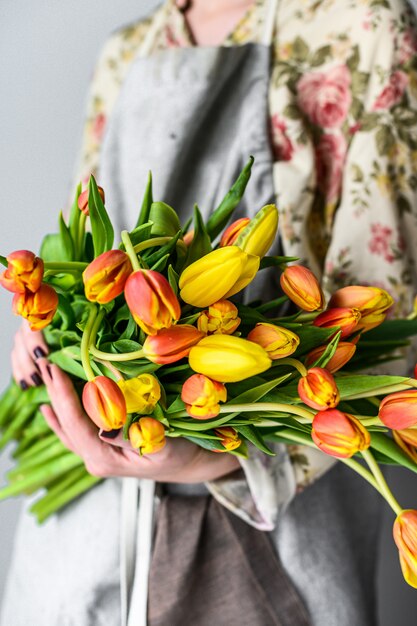 A girl holds a bouquet of yellow, orange and red Tulips. White background