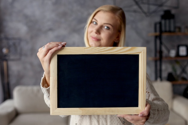 Girl holds a chalk board in the apartment. copyspace.