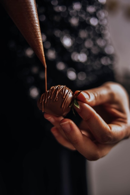 Foto la ragazza tiene in mano una fragola ricoperta di cioccolato e la decora versando la glassa