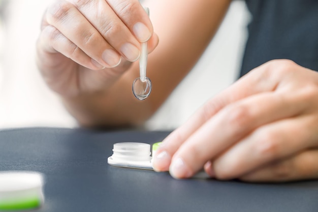 Girl holds contact lens with tweezers, black background, closeup