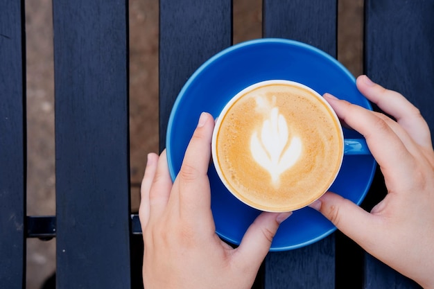 A girl holds a cup of cappuccino in her hands on a wooden table on a summer terrace