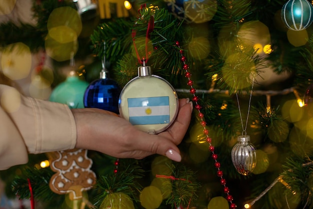 A girl holds a decoration on a Christmas tree with the flag of Argentina