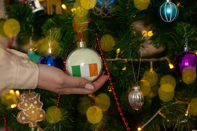 A girl holds a decoration on a Christmas tree with the flag of Ireland