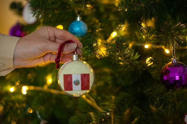 A girl holds a decoration on a christmas tree with the flag of peru