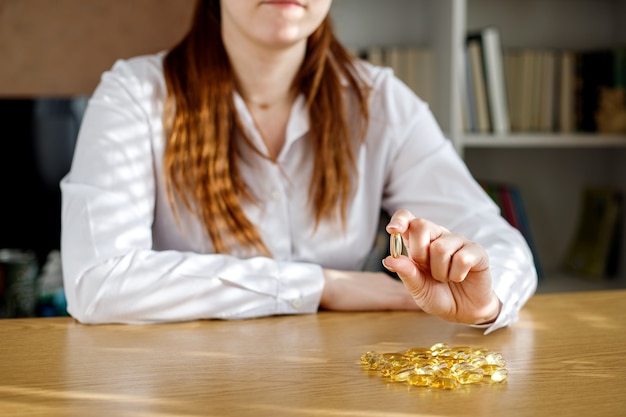 La ragazza tiene in mano una capsula di olio di pesce. capsule di omega-3 sul tavolo e in mano al medico.