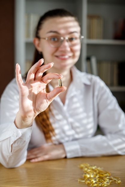 The girl holds a fish oil capsule in her hand. Omega-3 capsules on the table and in the doctor's hand.