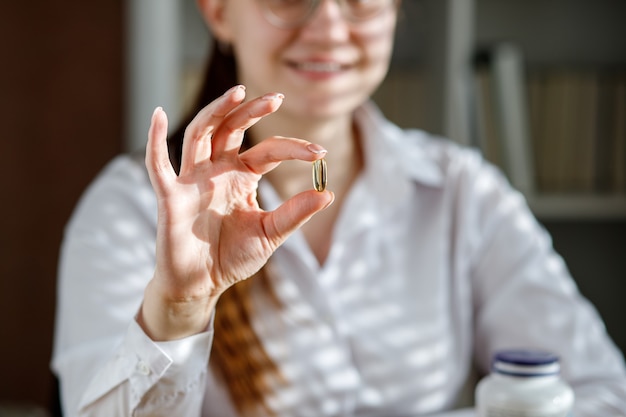 Photo the girl holds a fish oil capsule in her hand omega3 capsules on the table and in the doctors hand