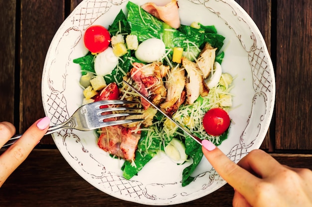 The girl holds a fork and a knife in his hands and starts to eat a delicious salad