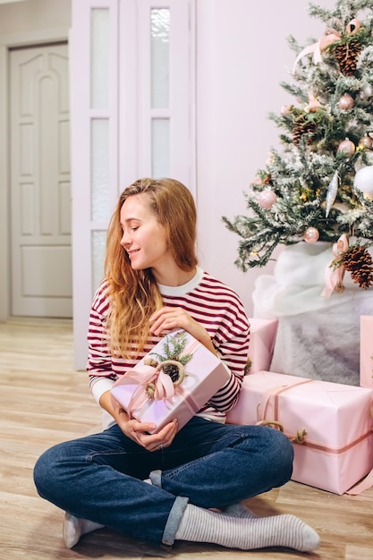 女の子は贈り物、クリスマスツリー、贈り物とピンクの箱を持っています