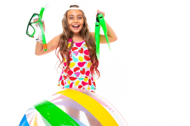 Girl holds glasses and scuba diving flippers near an inflatable ball on a white wall