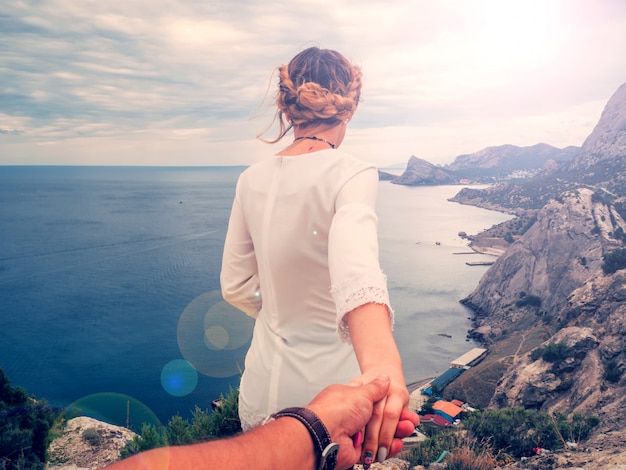 Girl holds her boyfriend's hand against the sea on a cliff on a summer day