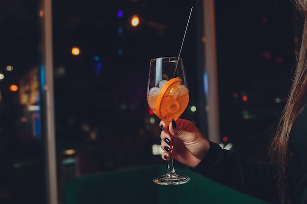 A girl holds in her hand a transparent glass of red cocktail, ice cubes float in the glass.