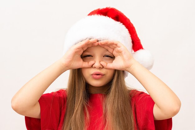 The girl holds her hands near her eyes in a Christmas hat.