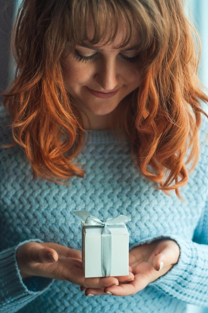 the girl holds in her hands a small box with a gift looks at her smiles happy from loved ones gratit