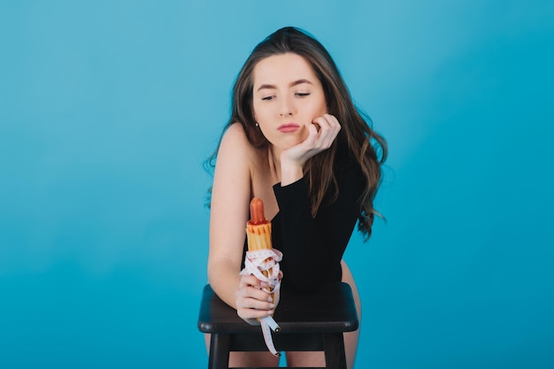 girl holds hot dog in hand with measuring tape on blue background